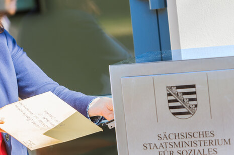 Ein Mensch steckt einen Umschlag in den Briefkasten des Staatsministeriums für Soziales und Verbraucherschutz.