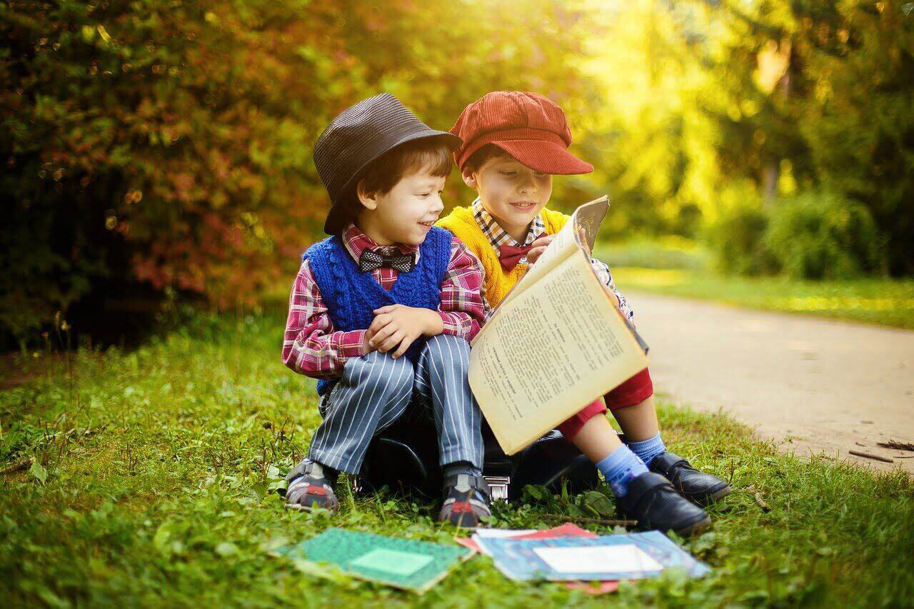 2 kleine Jungen sitzen auf der Wiese und halten Bücher in der Hand